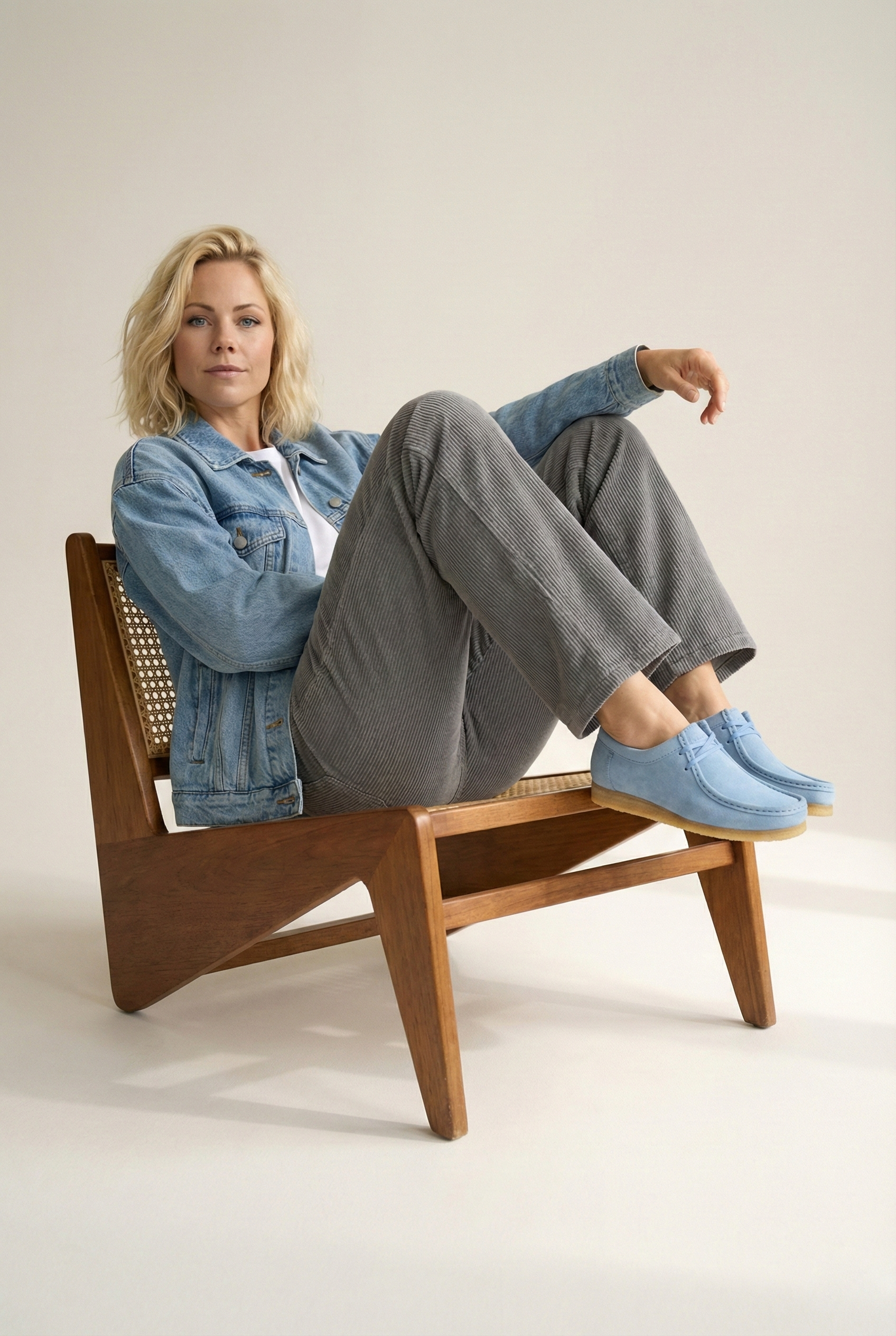 Woman sitting on a wooden chair wearing a denim jacket, gray pants, and grasshopper loafers/ moccasin in baby blue