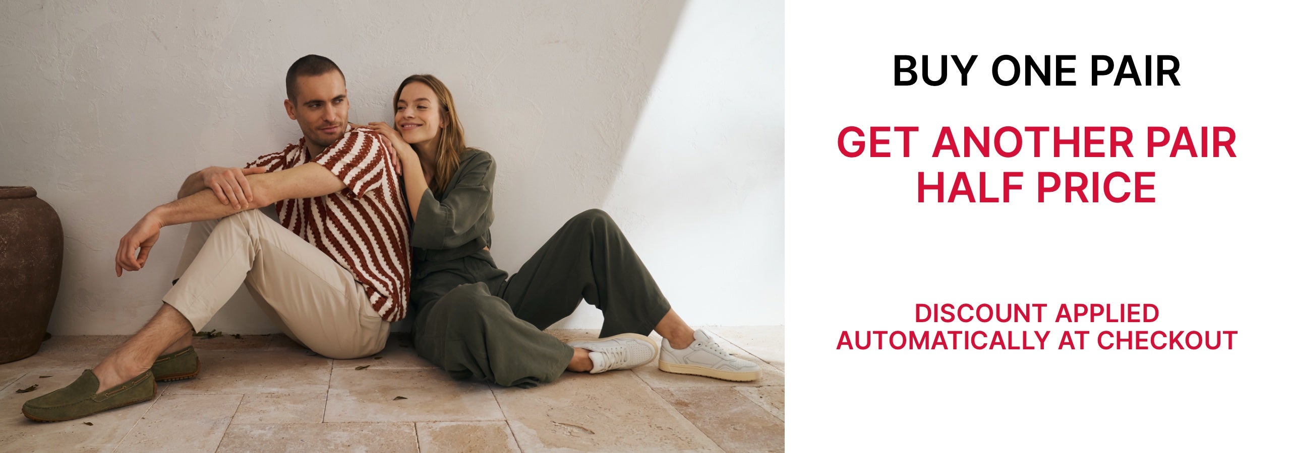 Two people sitting on a floor with a promotional banner for Buy One Pair, get another pair half price offer offer. The offer is automatically applied at checkout.
