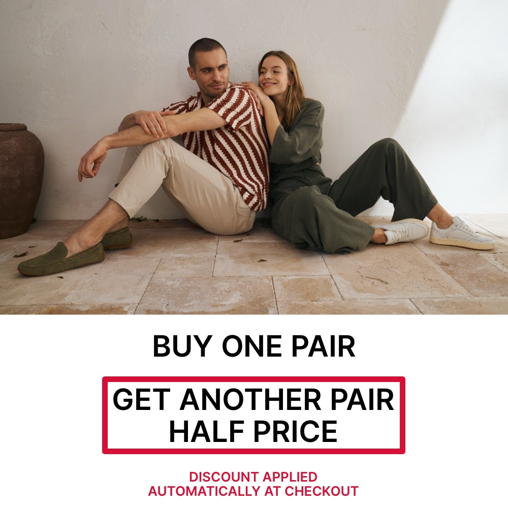 Two people sitting on a floor with a promotional banner for Buy One Pair, get another pair half price offer offer. The offer is automatically applied at checkout.
